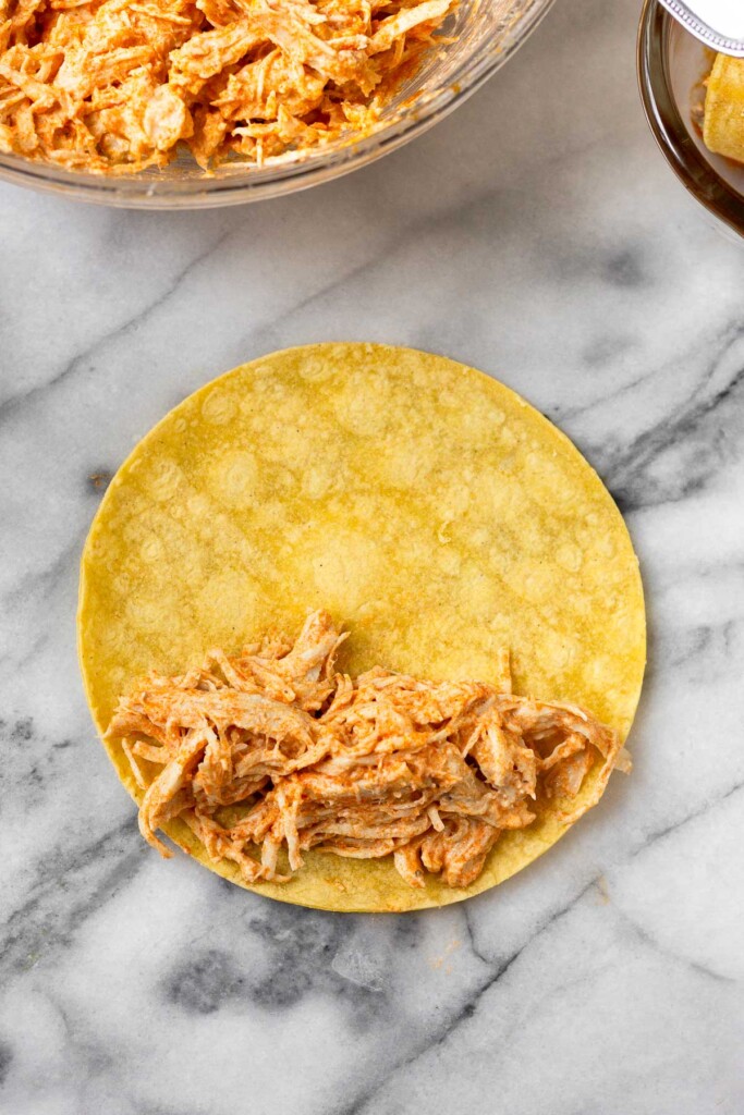 A corn torilla topped with a shredded chicken mixture on about half of it.