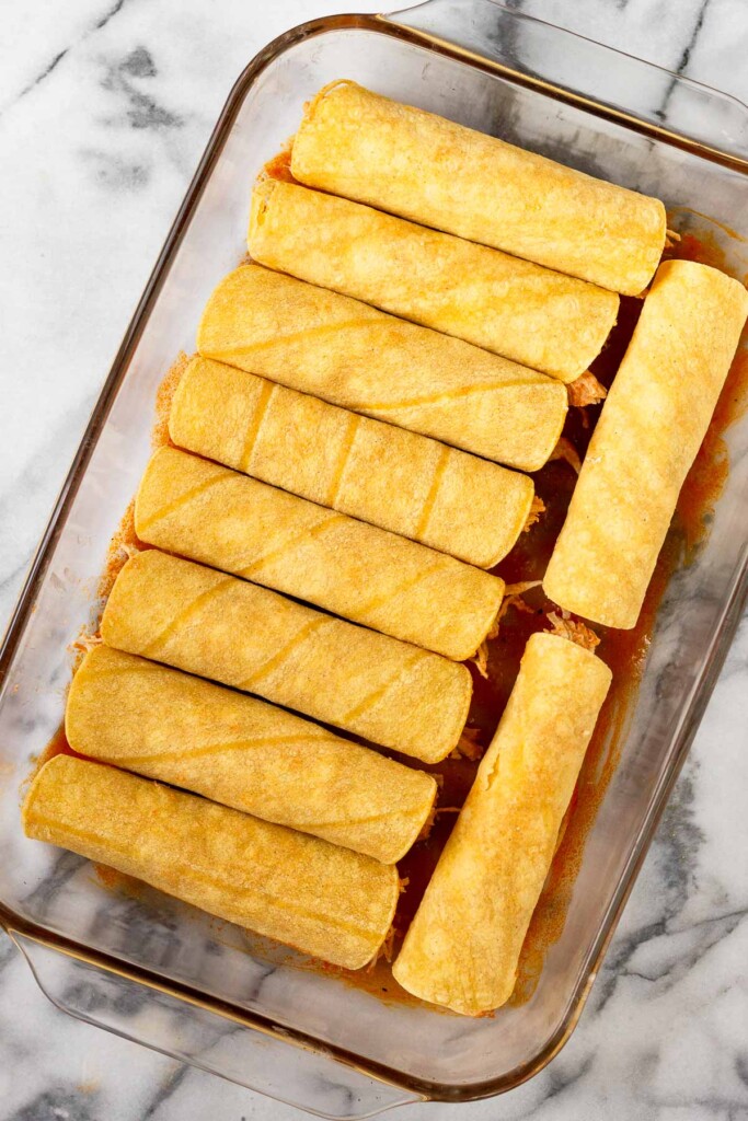 Casserole dish of rolled up chicken enchiladas in corn tortillas before any sauce is put on top.