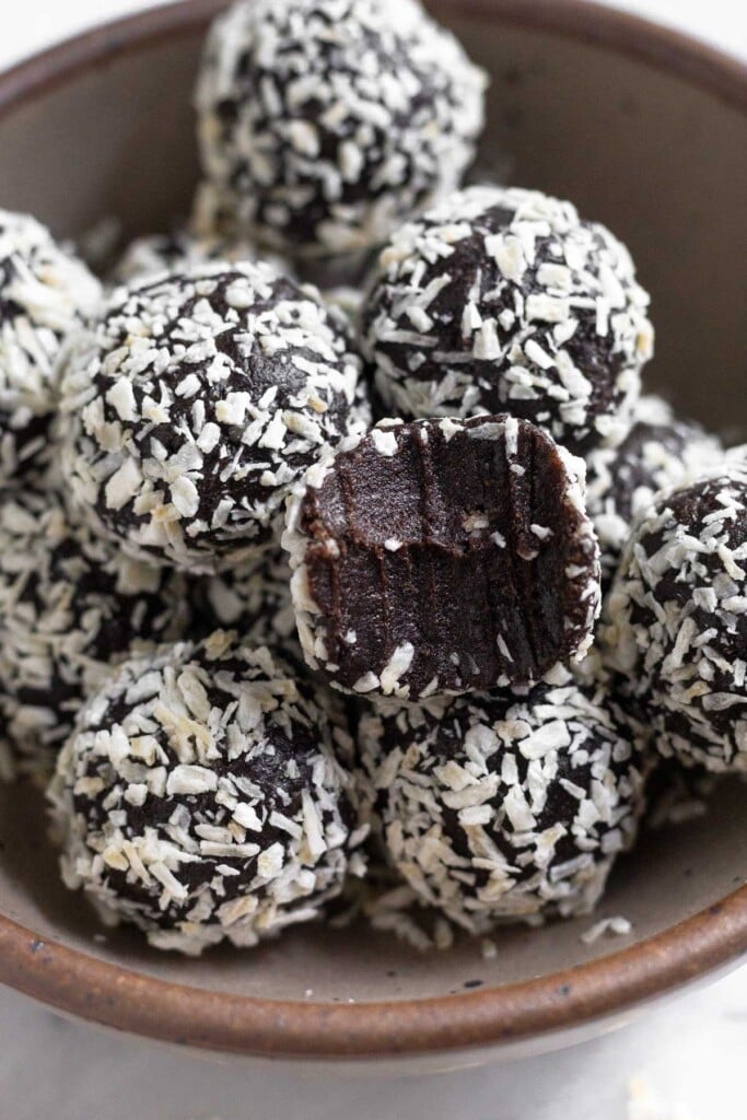 A bowl of chocolate peppermint energy balls coated with shredded coconut. One of them as a bite taken out of it.