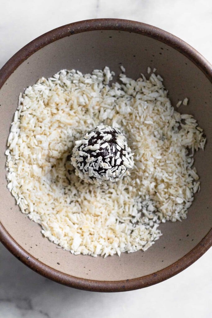 A small bowl of shredded coconut with a chocolate energy ball coated with coconut in it.