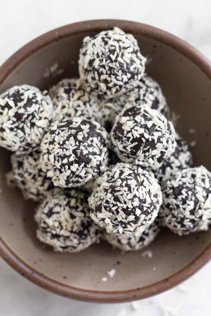 An overhead shot of chocolate peppermint protein balls coated with shredded coconut in a small brown bowl.