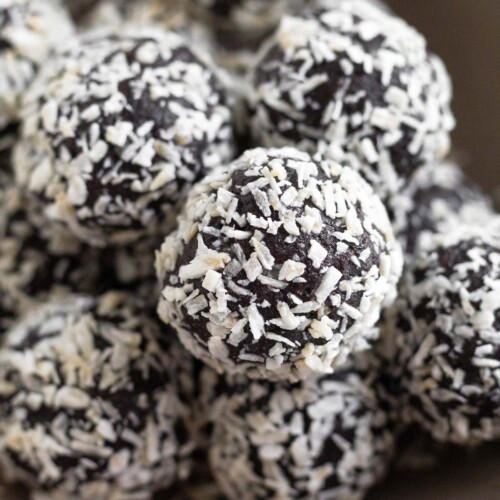 A pile of chocolate peppermint energy balls in a small brown bowl. They are coated with shredded coconut.