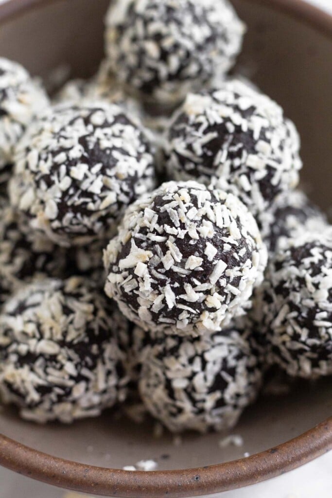 A pile of chocolate peppermint energy balls in a small brown bowl. They are coated with shredded coconut.