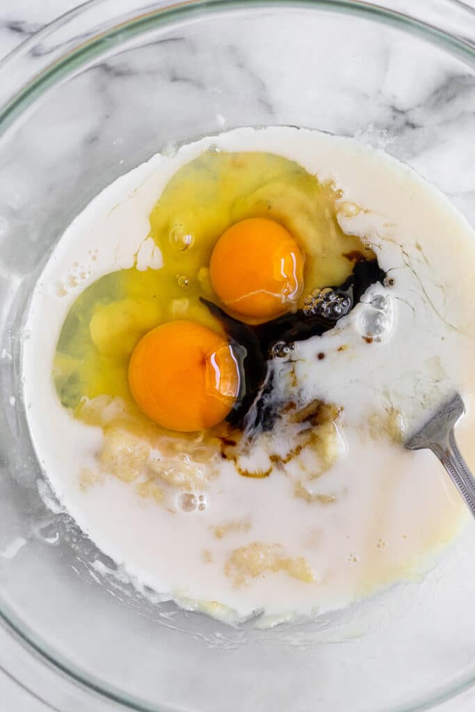 Bowl with mashed bananas, 2 eggs, almond milk, and molasses with a fork in it.