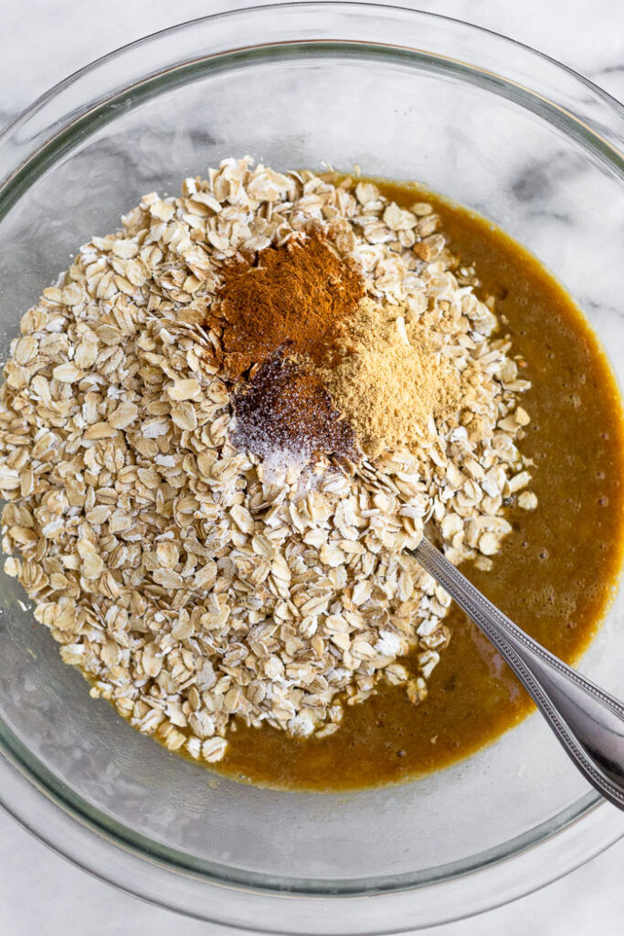 Large bowl with a mixture of mashed banana and almond milk. On top is a large pile of rolled oats and spice. There is a fork in the bowl as well.