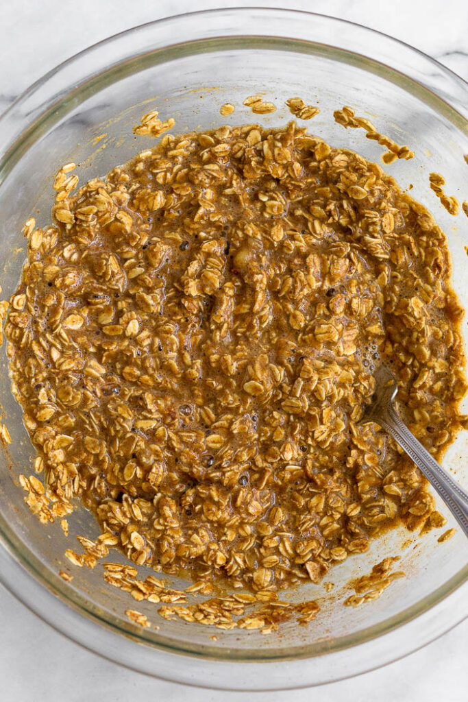 Large glass bowl with a mixture of mashed bananas, almond milk, oats, and spices all mixed together.