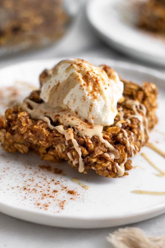 Close up a gingerbread oatmeal bar on a plate. It is topped with yogurt and nut butter and sprinkled with cinnamon.
