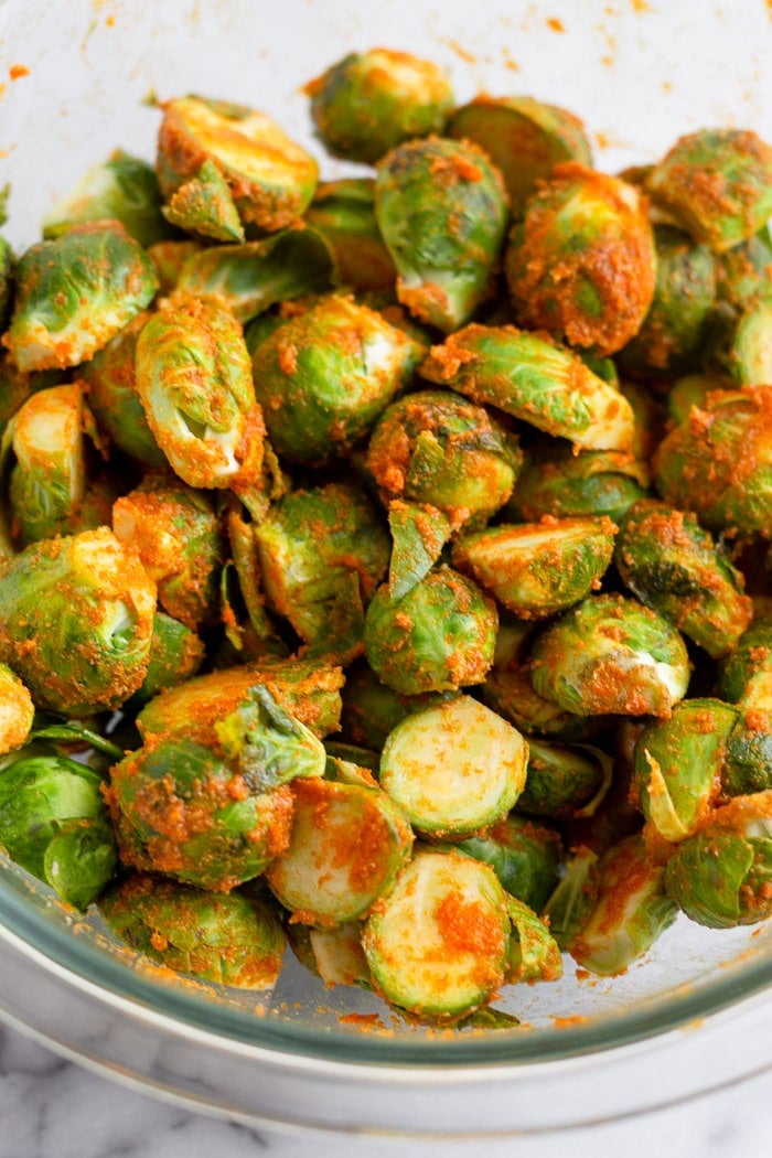 A bowl of brussel sprouts tossed in hot sauce, oil, and spices.