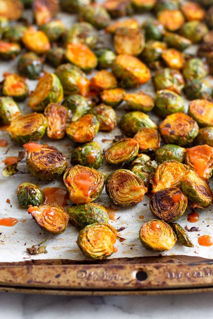 Buffalo roasted brussel sprouts on a baking sheet topped with hot sauce.