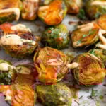 A bunch of buffalo brusssel sprouts topped with cheesy buffalo sauce and fresh dill on a baking sheet.