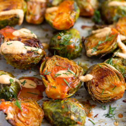 A bunch of buffalo brusssel sprouts topped with cheesy buffalo sauce and fresh dill on a baking sheet.