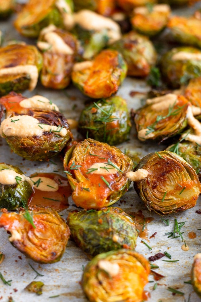 A bunch of buffalo brusssel sprouts topped with cheesy buffalo sauce and fresh dill on a baking sheet.