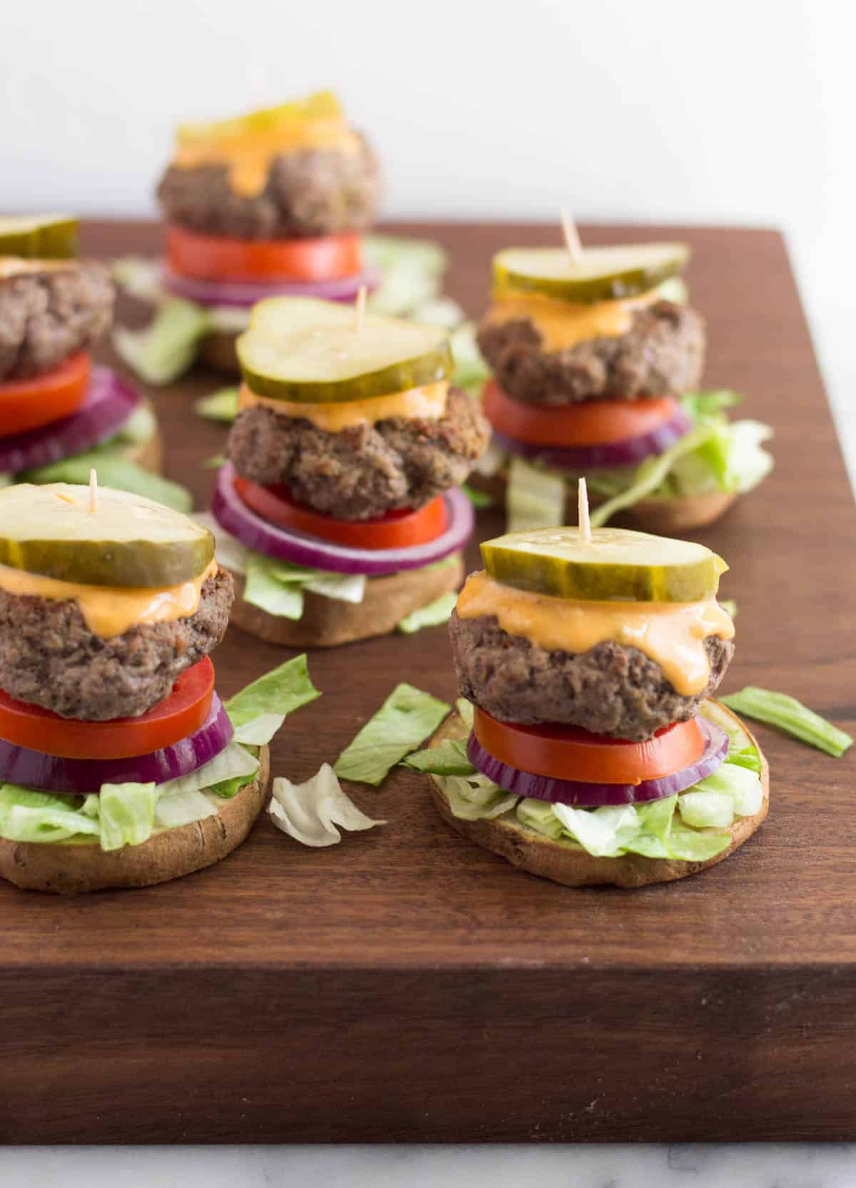 Butcher block with a lot of burger sliders on sweet potato buns on it
