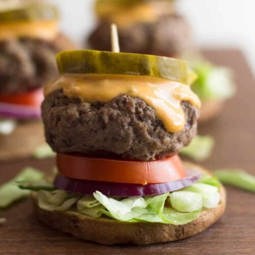 Close up of a beef slider on a sweet potato bun topped with lettuce, onion, tomato, special sauce, and a pickle