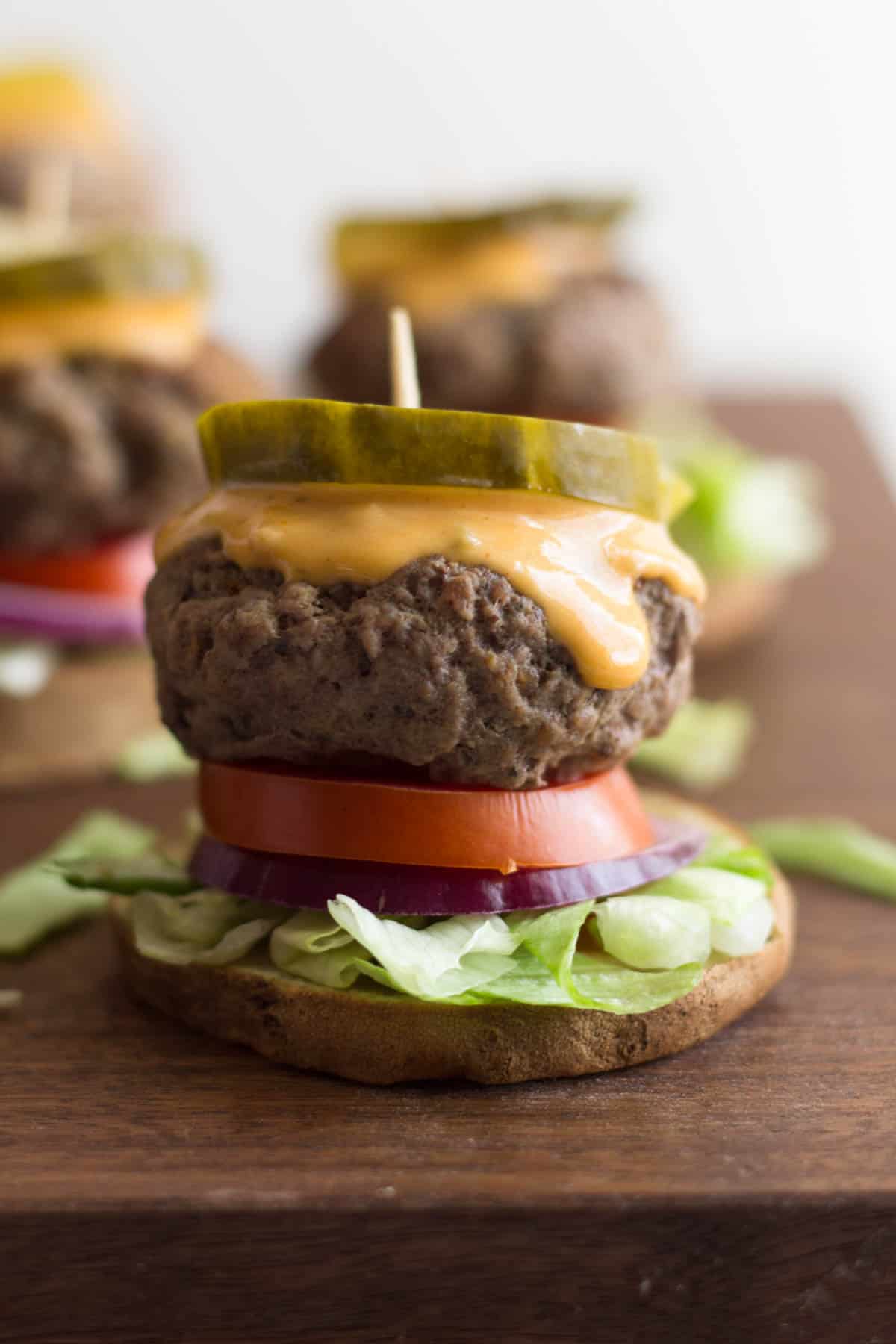 Close up of a beef slider on a sweet potato bun topped with lettuce, onion, tomato, special sauce, and a pickle