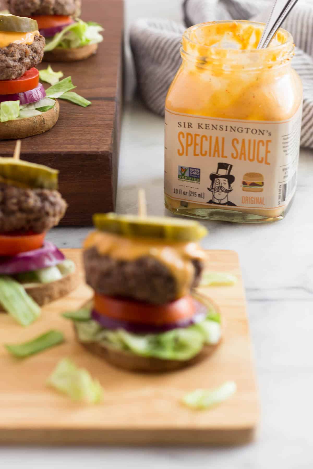 Burger slider on a sweet potato bun that is out of focus with a jar of special sauce that is in focus in the background