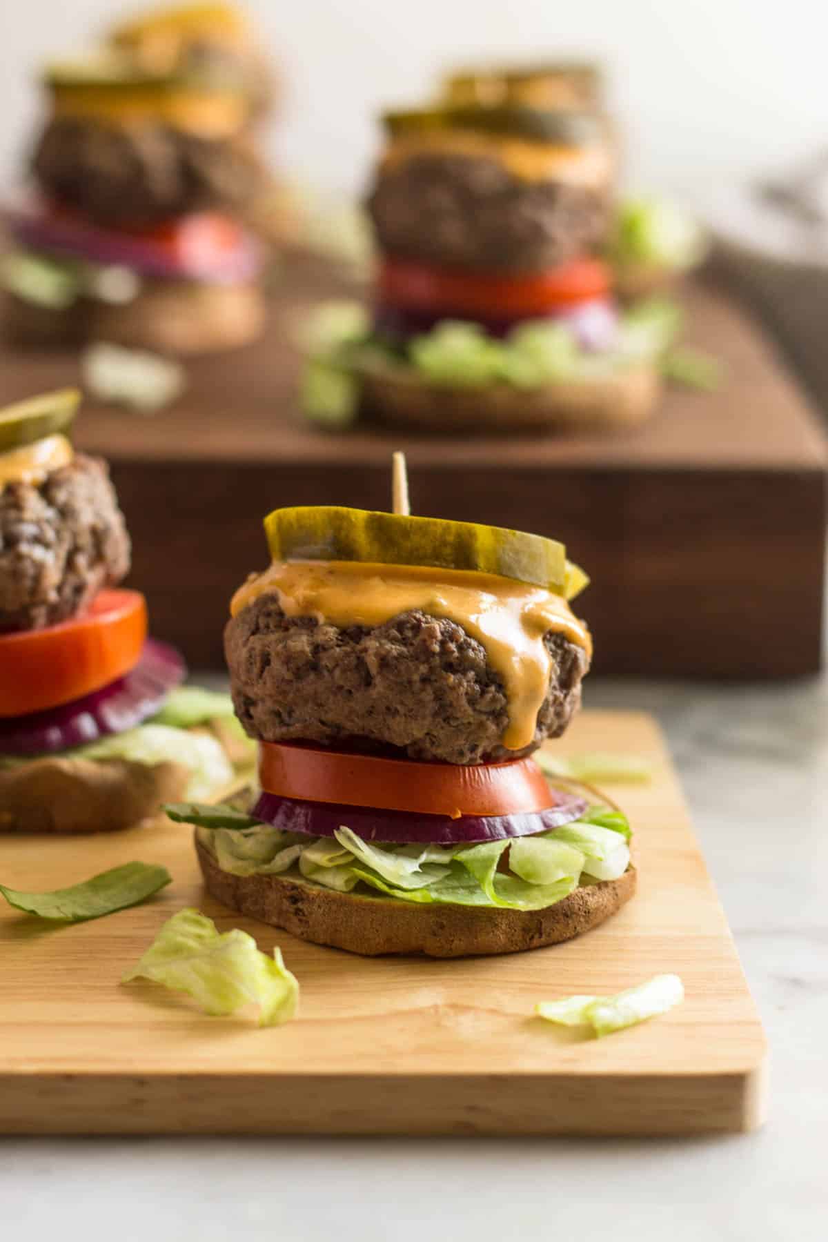Close up of a burger slider on a sweet potato bun on a wooden board with a lot of sliders in the background on a butcher block