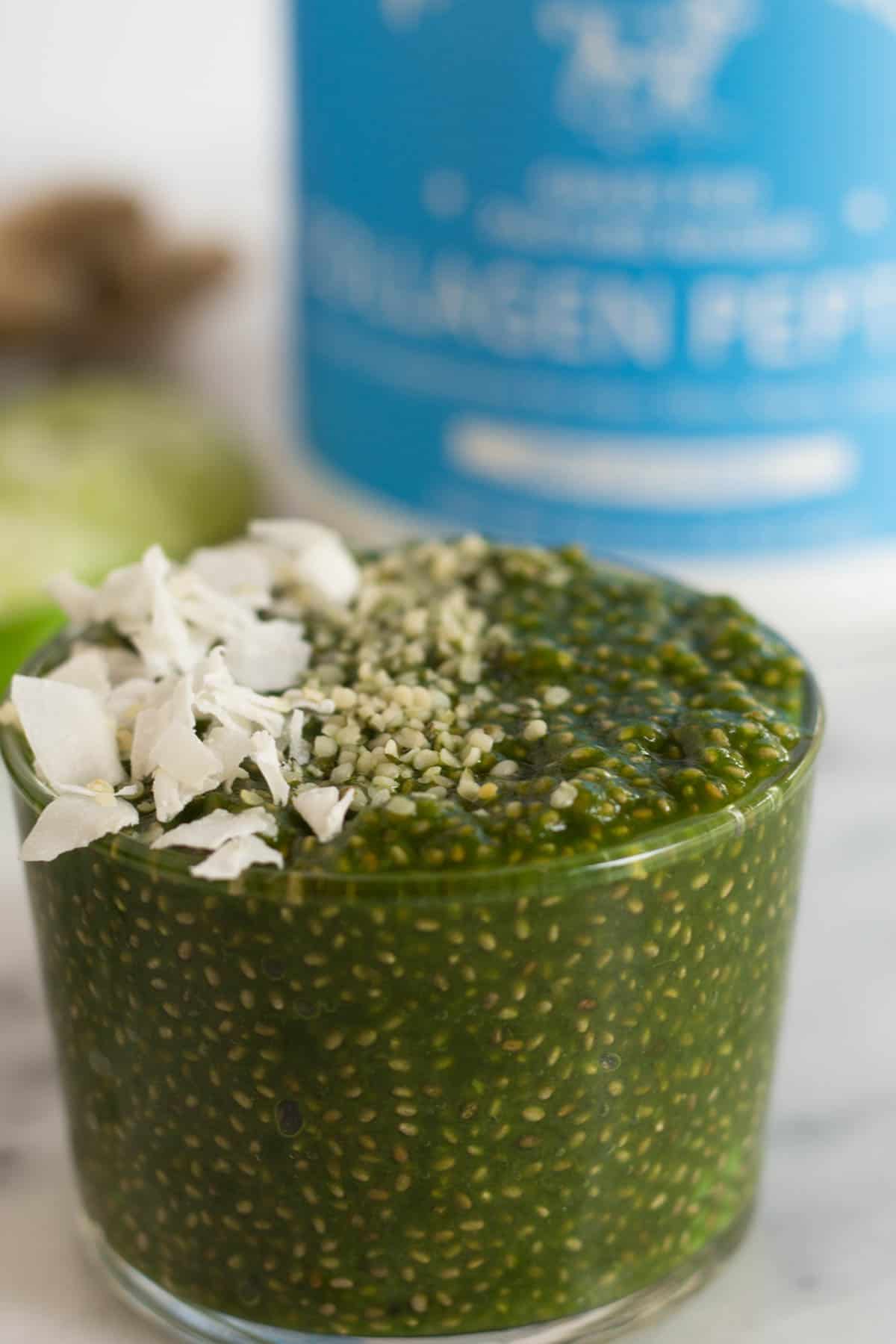 One glass of green juice chia pudding and a container of collagen in the background
