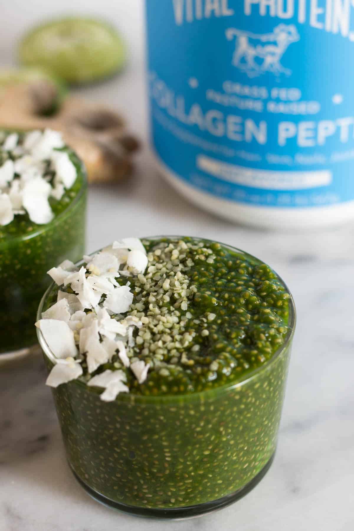 1 glass of green juice chia pudding with another glass and a container of collagen in the background