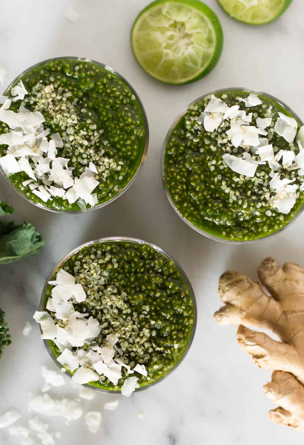 Overhead of 3 glasses of green juice chia puddings, ginger, and limes