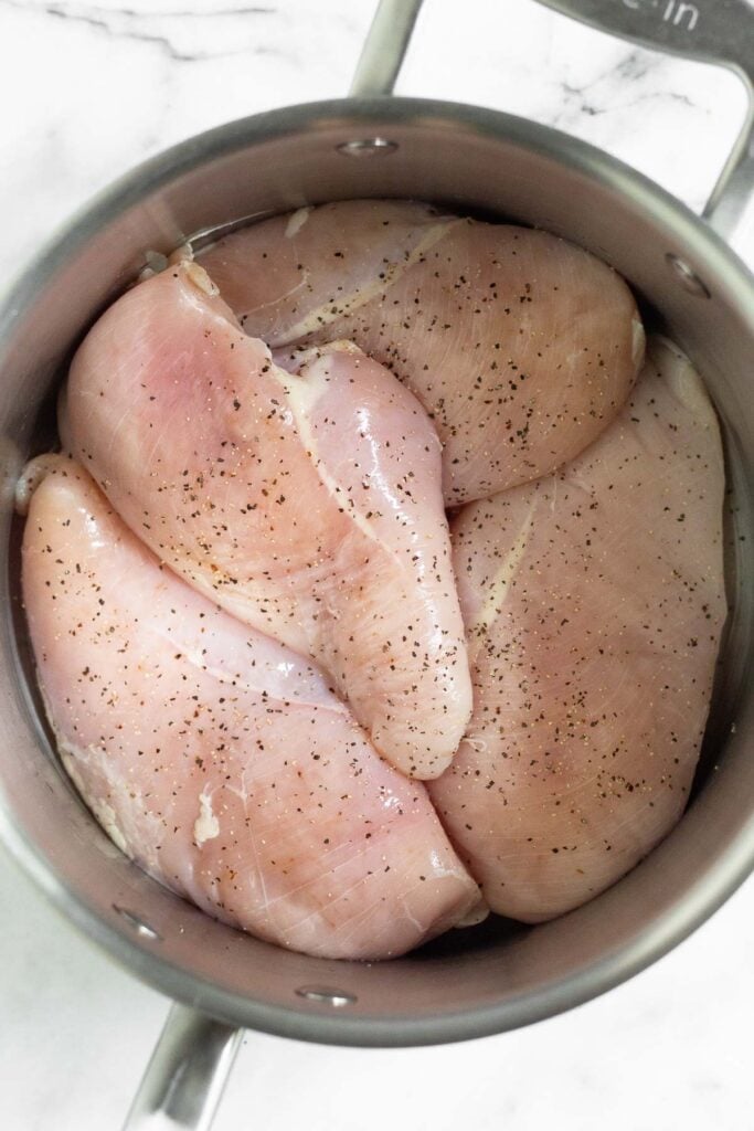 Stockpot filled with raw chicken sprinkled with salt and pepper.