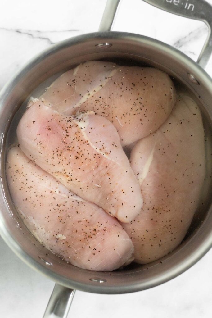 Stockpot filled with raw chicken sprinkled with salt and pepper. Water is covering the chicken.
