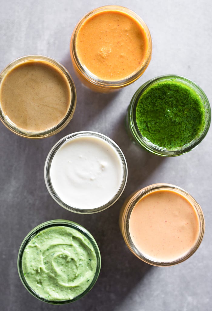 Overhead shot of 6 jars filled with different sauces on a grey table.