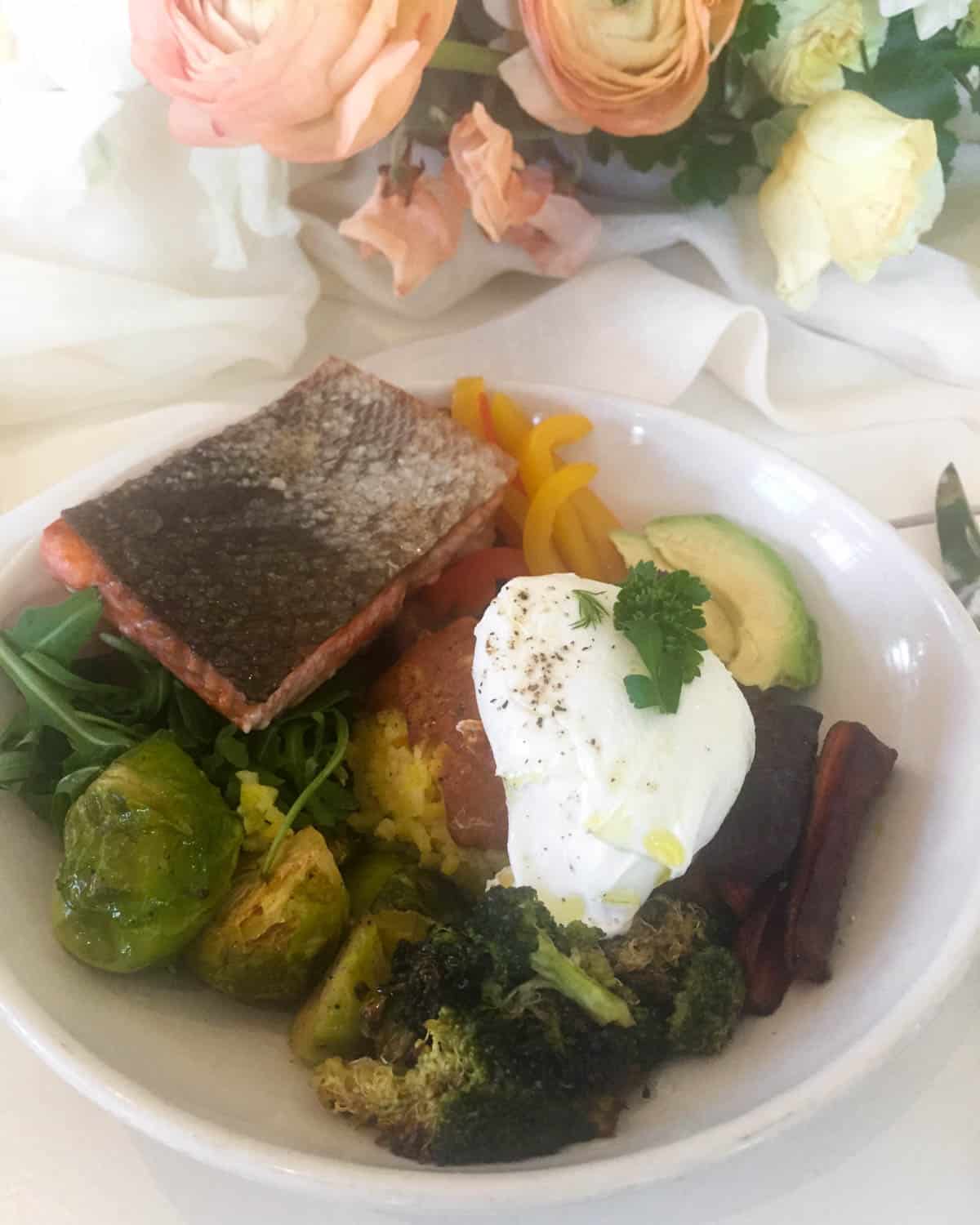 Bowl of roasted salmon, veggies, rice, avocado, and a poached egg on top
