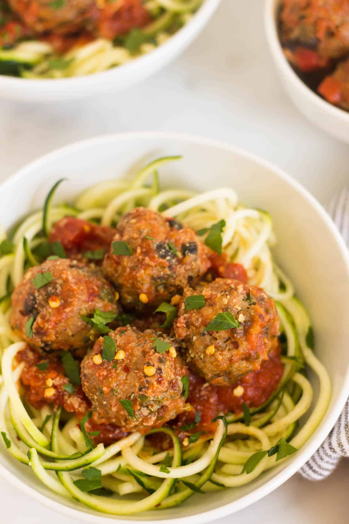 Close up of zucchini noodles with meatballs and sauce in a small white bowl
