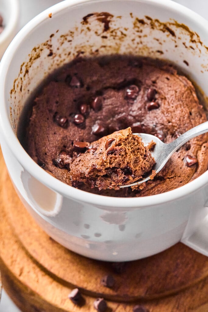Protein powder mug cake with a chocolate chips. A spoon with a spoonful of the cake is overtop the mug.