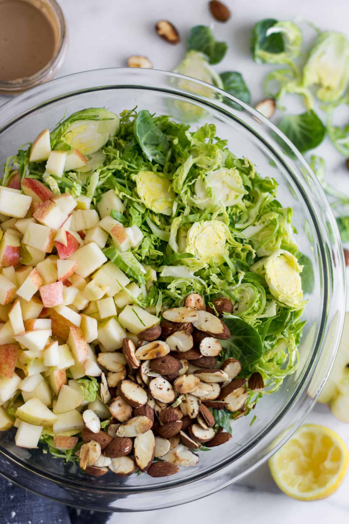 Glass bowl with shredded brussels sprouts, chopped apple, and toasted almonds