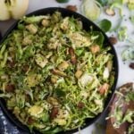 Big bowl with apple & shaved brussels sprouts salad surrounded by half an apple, half a lemon, brussels sprouts leaves, and almonds