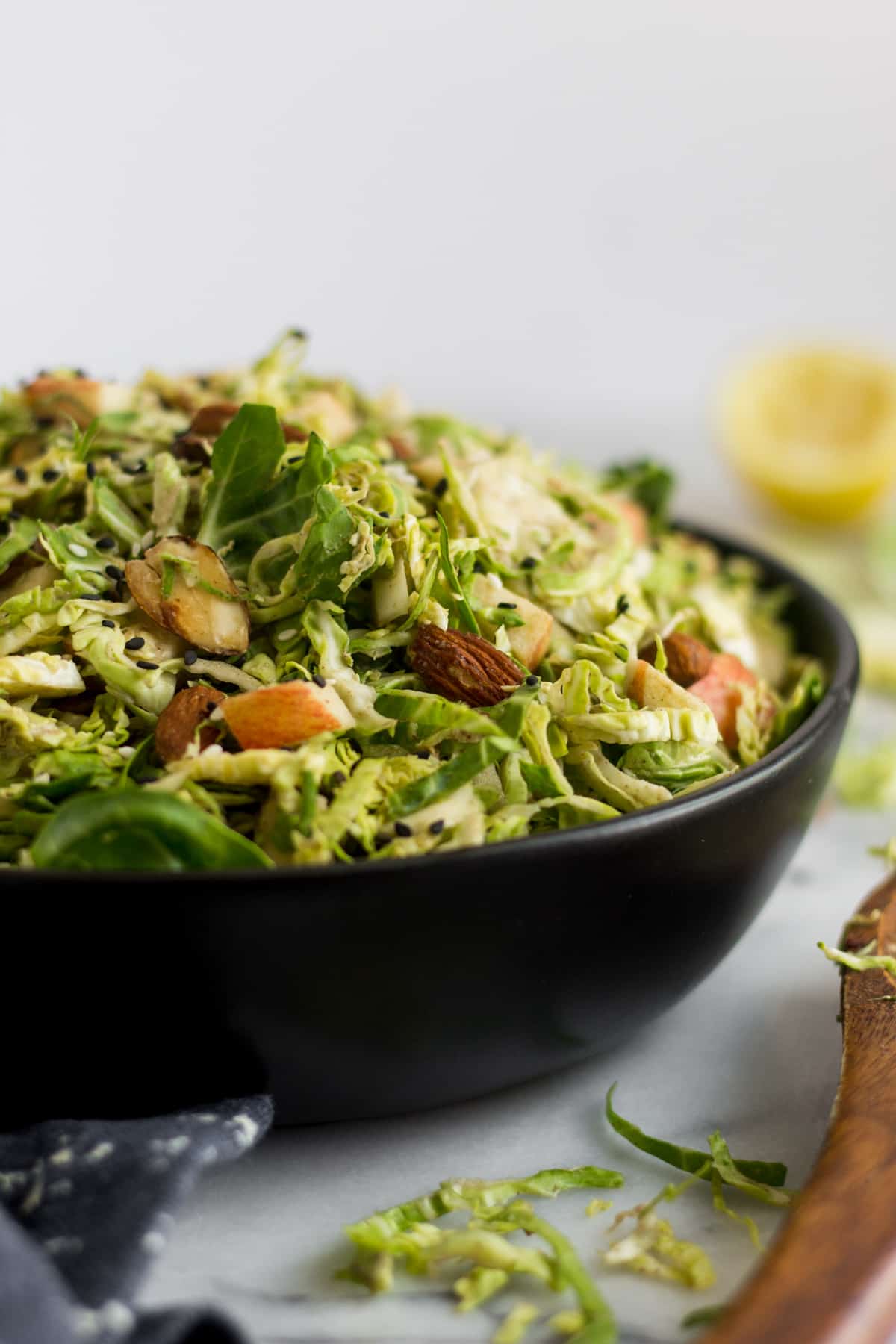 Straight on shot of a black bowl overflowing with apple & shaved brussels sprouts salad