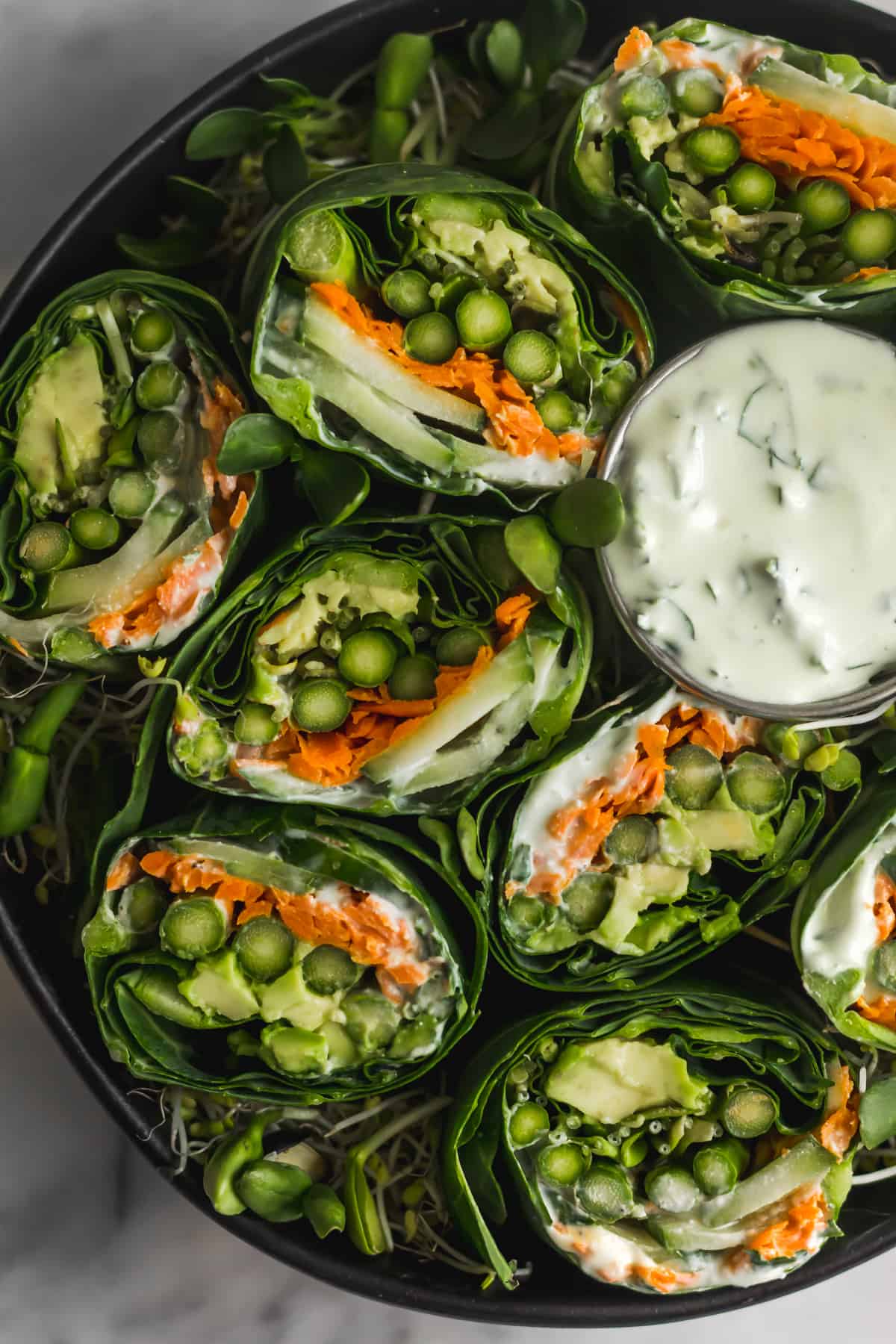 Overhead shot of a bunch of asparagus collard wraps in black bowl with a small cup of whipped feta