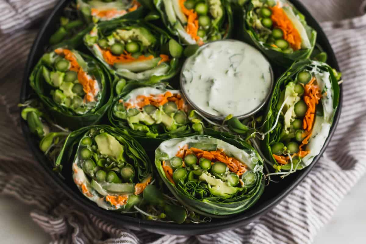 Close up of mini asparagus collard wraps in a large bowl with a container of whipped feta in the bowl