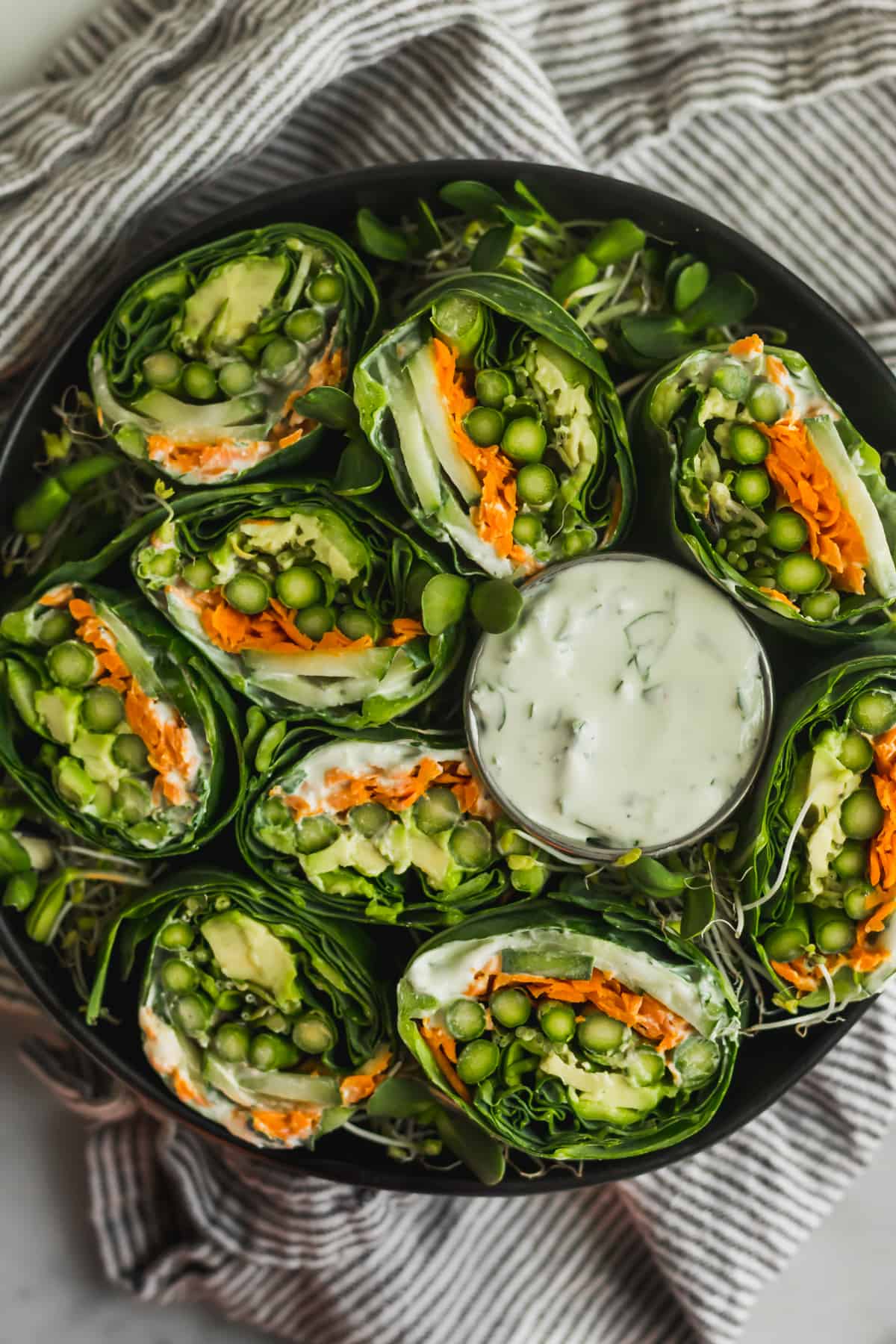 Large black bowl over a stripped towel filled with vegetarian collard wraps