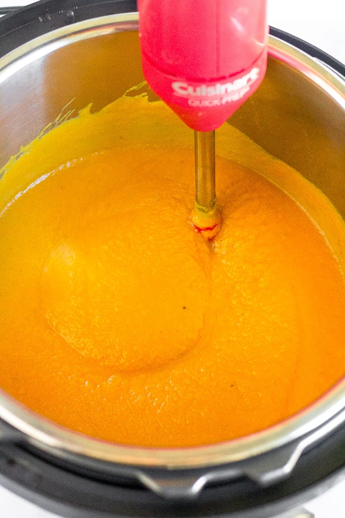 Instant Pot filled with curried cauliflower soup with an immersion blender in it blending it.