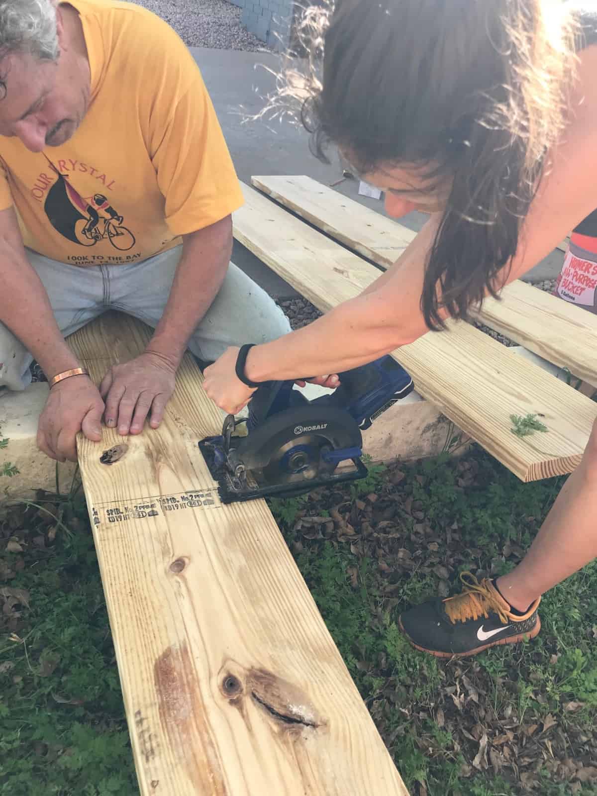 Girl with a power saw cutting a wooden board with a guy holding it