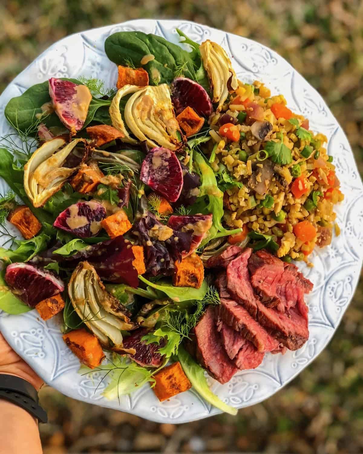 Plate of a big salad with greens, roasted fennel, blood oranges, and sweet potatoes, steak, and broccoli fried rice