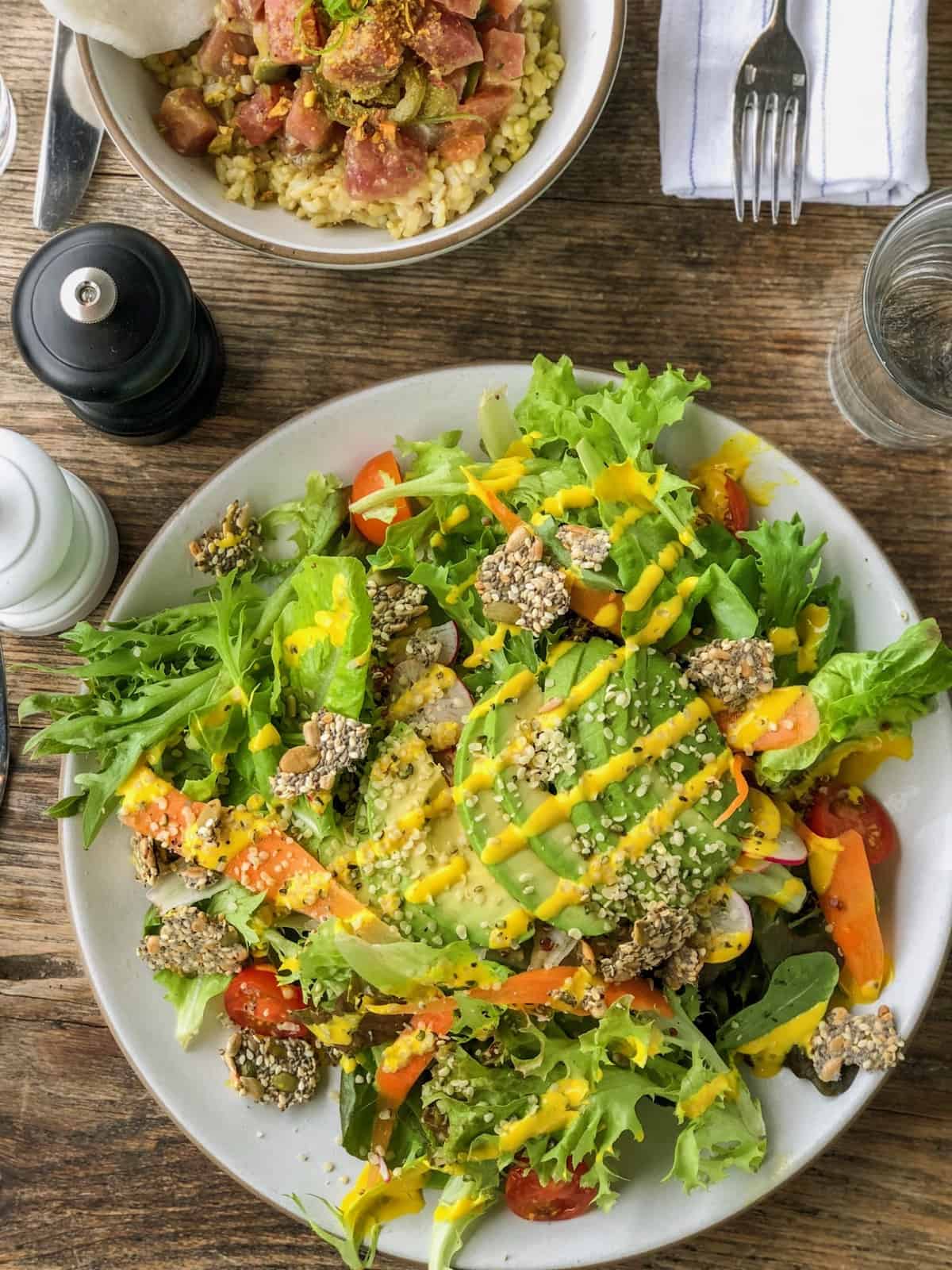 Salad topped with fresh veggies, avocado, and a turmeric tahini dressing