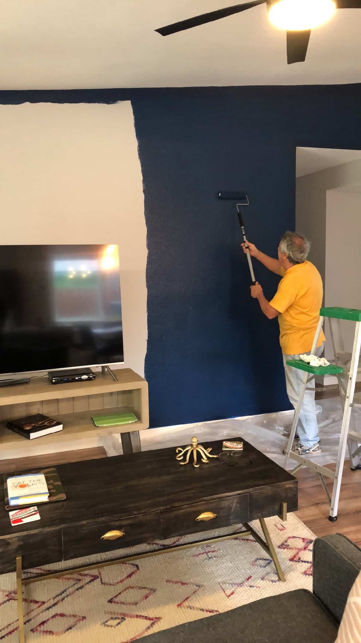 A guy painting a wall dark blue in a living room