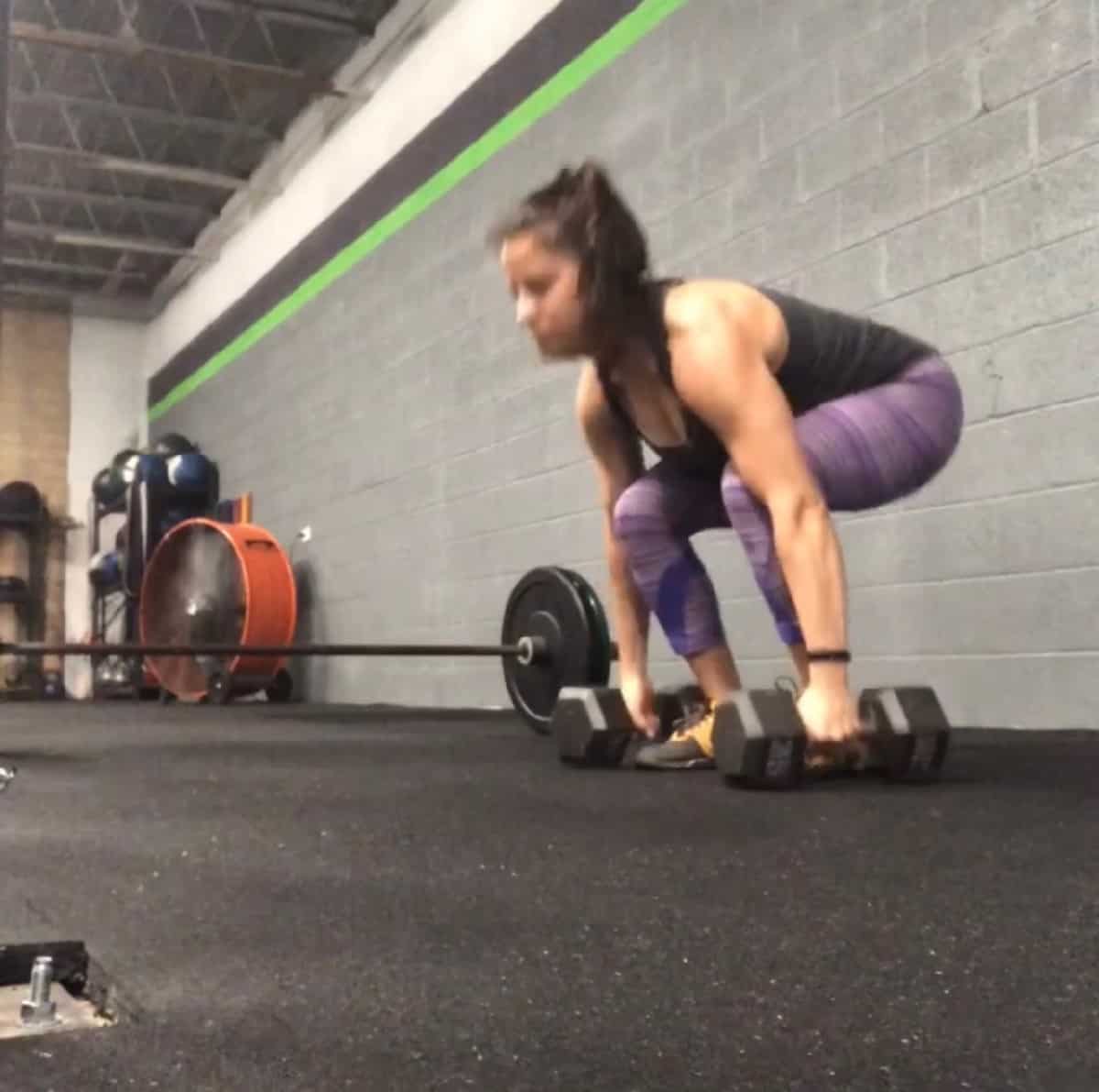 Girl squatting holding two dumbbells on the floor
