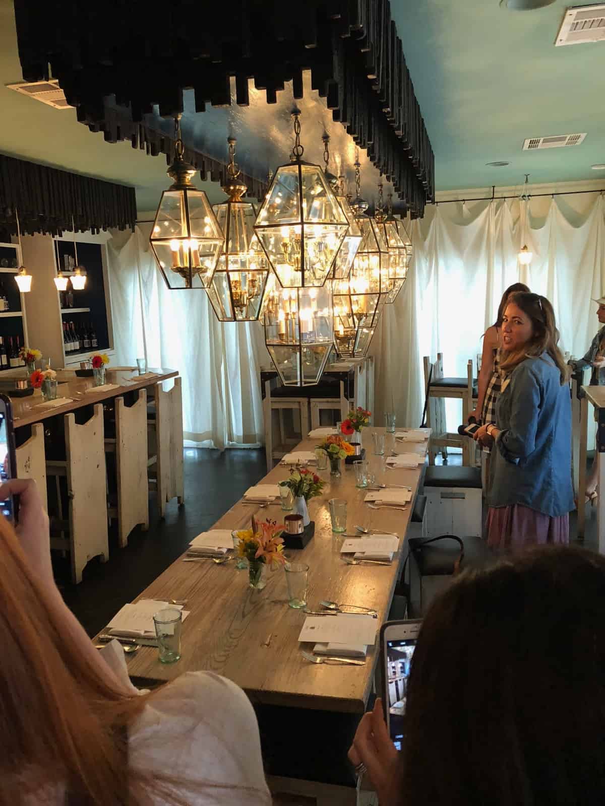 The inside of of Lenior restaurant with a long wooden table and different chandeliers above it