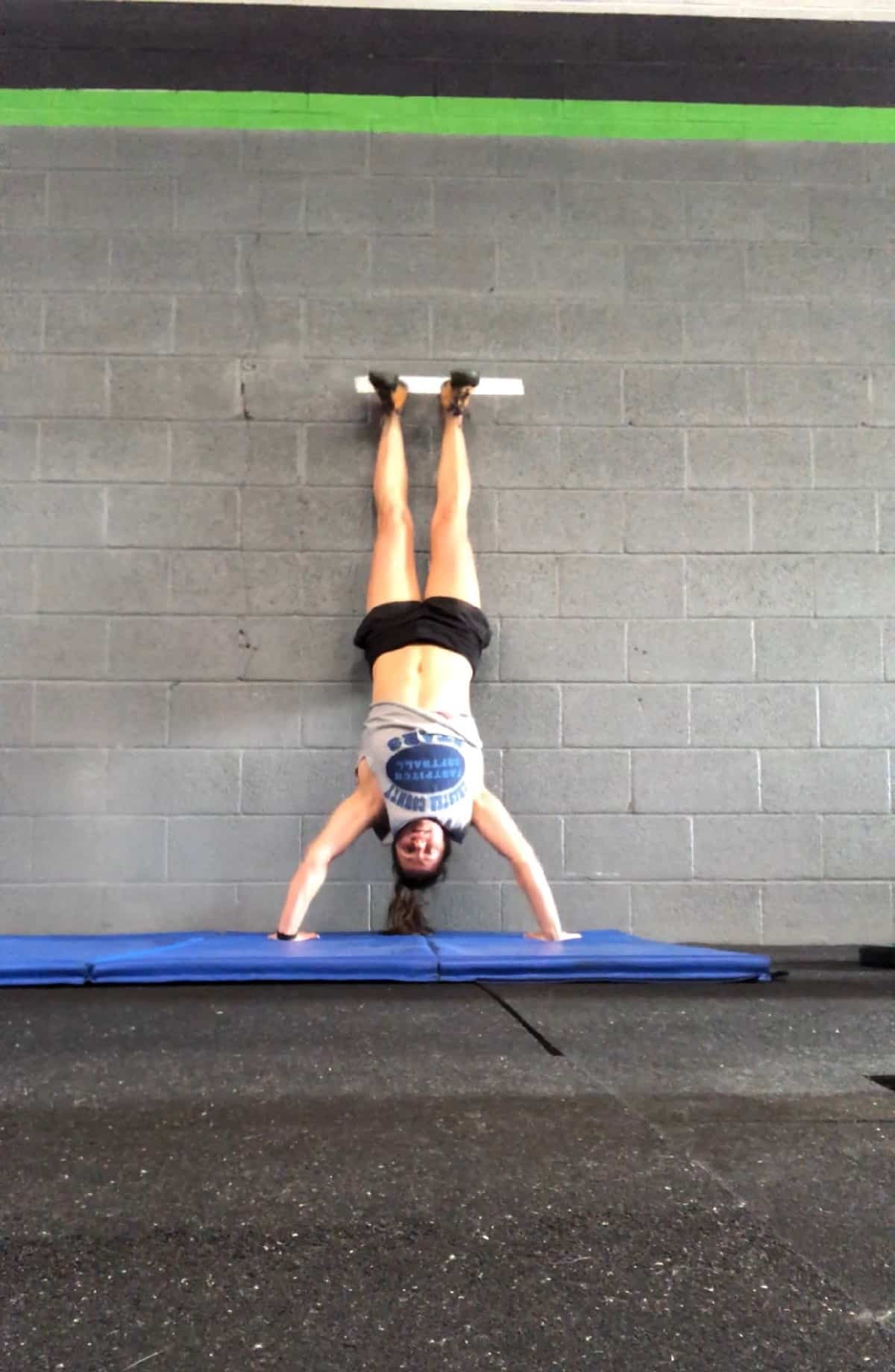 Girl upside-down against a wall doing a handstand push-up