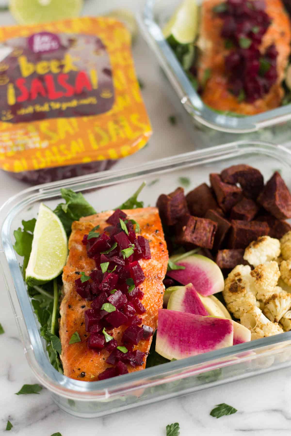 Glass container with veggies and pan fried salmon with another container in the back filled withe the same thing and a package of precooked beets