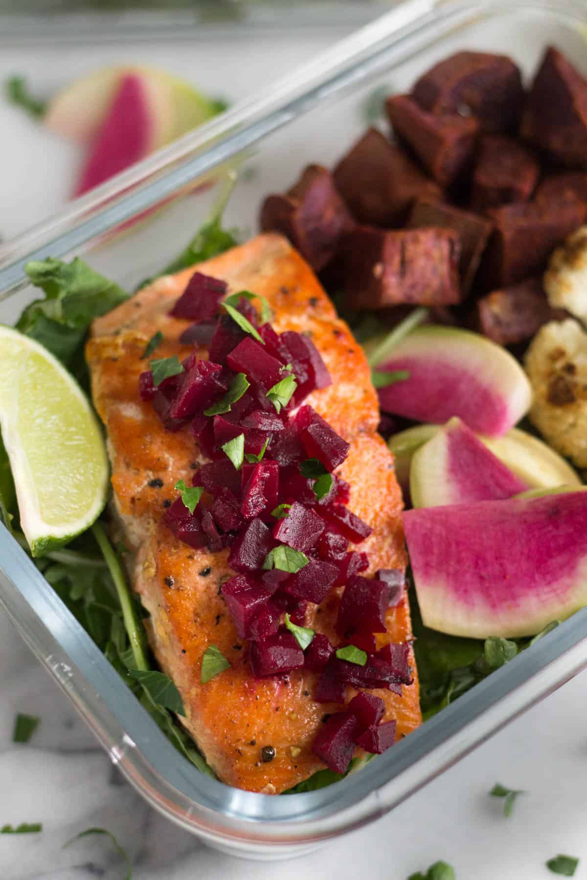 Close up of pan friend salmon topped with chopped beets and other veggies in a glass container