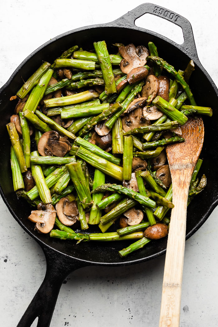 Sautéed asparagus and mushrooms in a skillet with a wooden spoon in it.