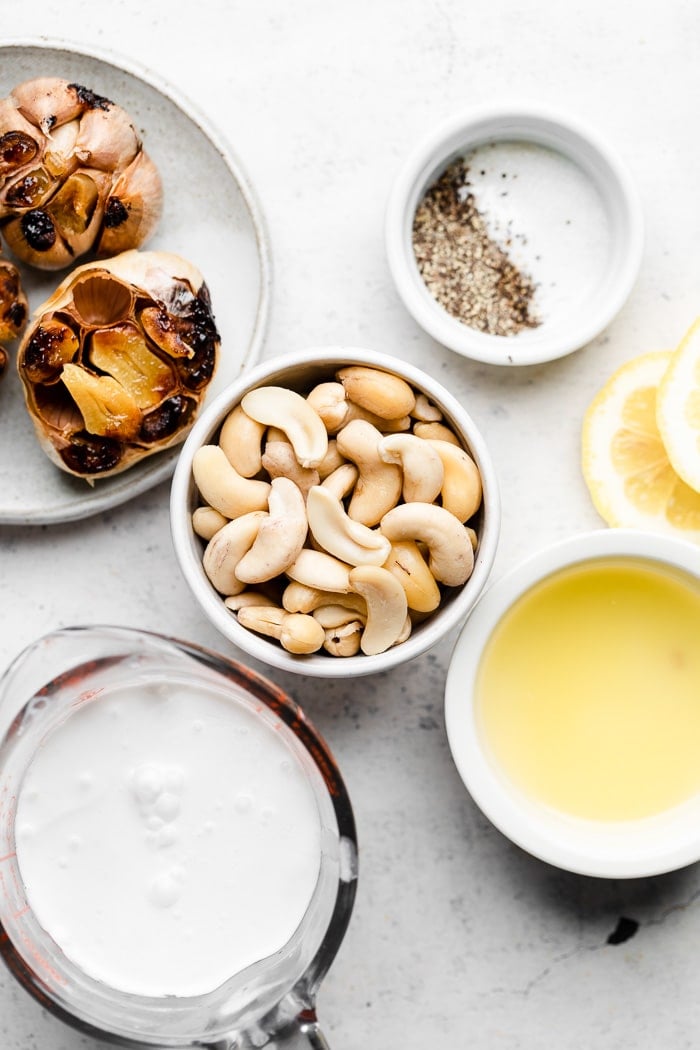 Overhead shot of roasted garlic, while cashews, salt and pepper, lemon juice, and coconut milk.