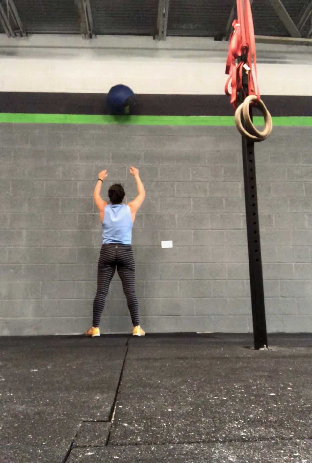 Girl throwing a med ball in the air against the wall doing a wall ball