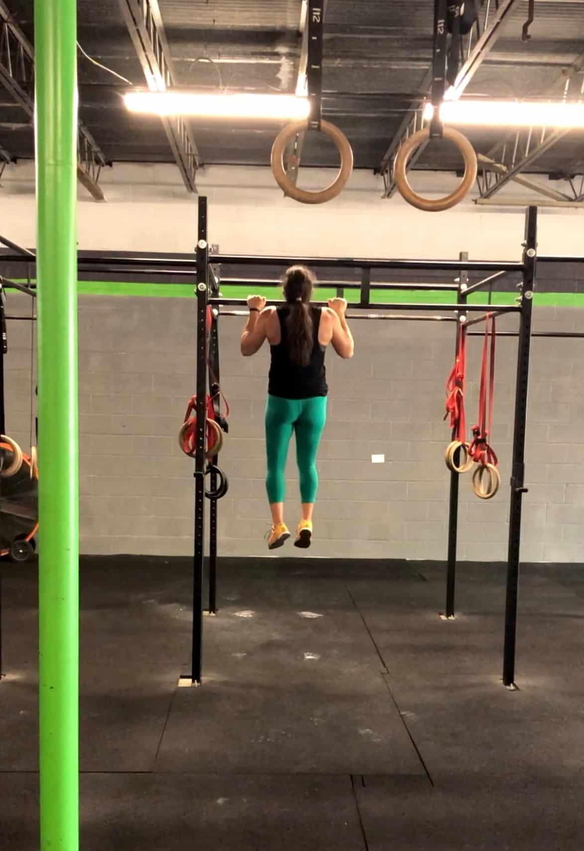 Girl in green leggings doing a strict pull-up